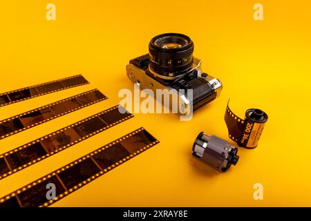 Gros plan d'un vieil appareil photo avec des rouleaux de film 35 mm usagés sur fond jaune, capturant l'essence de la photographie analogique. Banque D'Images