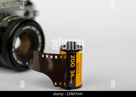 Un rouleau de film 35 mm à la mise au point nette avec un appareil photo à l'ancienne, dépourvu d'objectif, légèrement flou derrière lui. Le fond blanc accentue le classi Banque D'Images