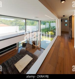 Couloir avec parquet et balustrade en verre. En bas, vous pouvez voir le salon. Grandes fenêtres donnant sur le jardin et le balcon. Personne Banque D'Images