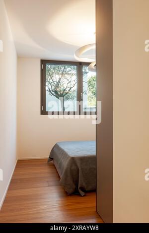 Détail d'une chambre dans une villa moderne. Vue depuis le couloir où vous pouvez voir le lit et une fenêtre lumineuse donnant sur le jardin. Personne à l'intérieur Banque D'Images