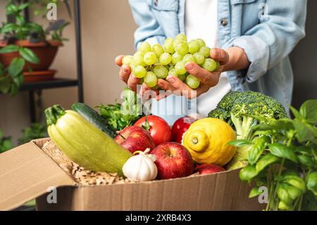 Personne déballer la commande en ligne de fruits et légumes cultivés à la ferme, tenant des raisins blancs dans ses mains. Banque D'Images