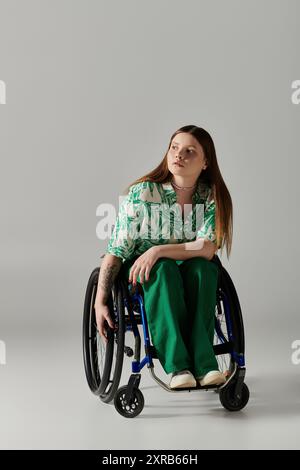 Une jeune femme, vêtue de vert, est assise dans un fauteuil roulant sur un fond gris. Banque D'Images