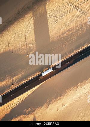 Véhicule sur une longue route droite en asphalte à la verticale vue - concept de transport et de voyage - désert de sable sol des deux côtés - ombres au coucher du soleil Banque D'Images