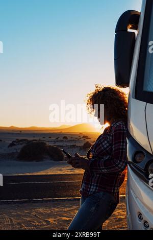 Personnes en voyage avec camping-car moderne. Femme utilisant l'itinérance de téléphone mobile contre le grand camping-car. Concept de style de vie moderne et voyageurs. Vacances et vanlife envoyer un message avec cellulaire. Connexion Internet partout Banque D'Images