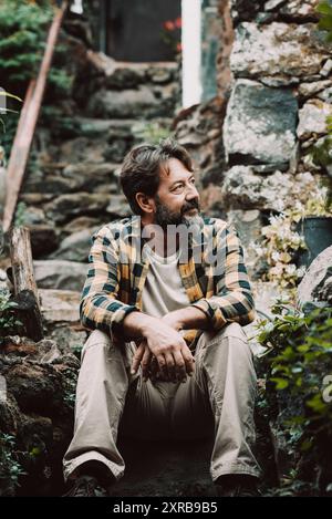 Hipster plein air mature barbu homme assis sur un escalier de rochers et appréciant la nature autour de regarder et de se reposer - simple homme concept de style de vie - se détendre et se sentir avec la nature - homme adulte s'asseoir à l'extérieur Banque D'Images
