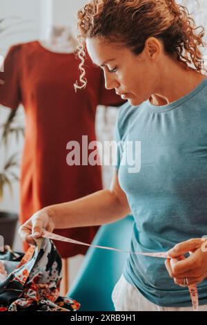 Femme travaillant à la maison dans la confection de studio créatif diy hobby. Les femmes adultes ont du temps libre à l'intérieur. Les gens travaillent en appartement. Dame prendre la taille des vêtements pour réparer ou modifier. Indépendance professionnelle moderne Banque D'Images