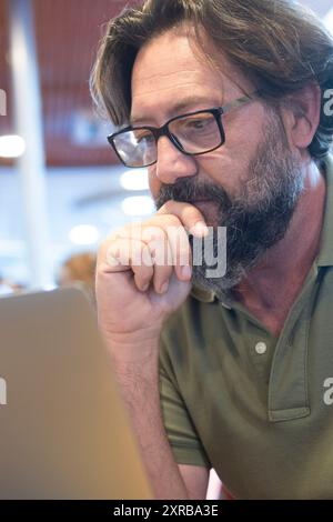 Portrait d'un homme travaillant sur un ordinateur portable dans un autre bureau de magasin. Les gens et la technologie moderne travail informatique activité de loisirs. Mûrissent avec la barbe et les lunettes en utilisant le carnet à la table. Porte arrière de l'aéroport Banque D'Images