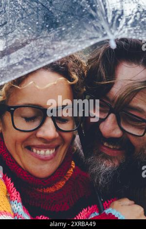 Amour entre l'homme adulte et la femme s'amusant ensemble sous un parapluie transparent dans le jour de pluie de l'activité de loisirs en plein air. Couple heureux en relation sous la pluie en automne ou en hiver Banque D'Images