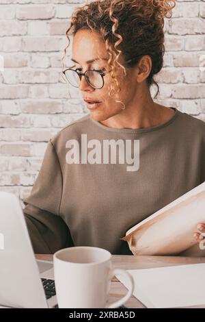 Étudiant mature utilisant un ordinateur et des papiers à la maison au bureau. Femme de bureau travaillant sur un ordinateur portable avec connexion. Portrait confiant des femmes et de l'activité professionnelle moderne. Architecte dame dans le studio Banque D'Images
