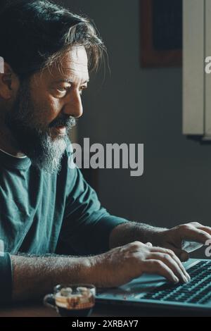 Bourreau de travail masculin mature impliqué dans le travail des heures supplémentaires, type lettre de rapport sur ordinateur portable, données de recherche sur le Web. Ambitieux jeune homme dans le travail intelligent développer la carrière passer du temps libre sur l'ordinateur à la maison seul à l'intérieur Banque D'Images