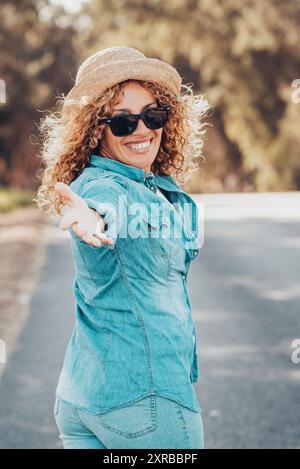 Portrait d'un merveilleux modèle féminin blanc avec des cheveux blonds bouclés exprimant l'énergie lors d'une bonne journée en Europe. Belle femme bouclée souriant et marchant avec des arbres derrière elle. Banque D'Images