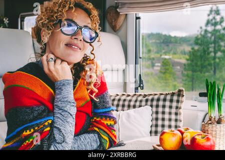 Une femme voyageuse heureuse profiter de vanlife liberté style de vie seul assis à l'intérieur du camping-car moderne. Vue sur le parc à l'extérieur de la fenêtre. Vivre hors réseau sur le voyage. Location de véhicule de camping-car concept de vacances. Aventure Banque D'Images