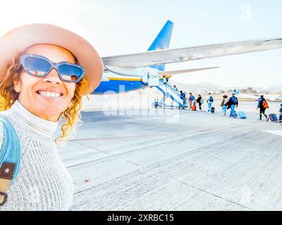 une femme de 50 ans portant un chapeau et des lunettes de soleil prend selfie avant d'embarquer dans l'avion. Happy Lonely Woman prend une photo souvenir. Banque D'Images