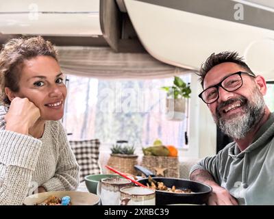 Heureux couple mangeant ensemble à l'intérieur d'un camping-car camping-car vivant la vie vanlife et voyage aventure vacances. Vie nomade. Homme et femme joyeux prenant selfie et souriant à la caméra Banque D'Images