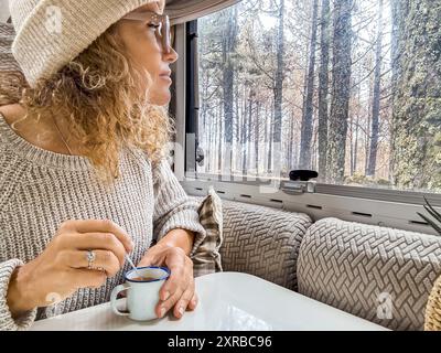 Belle femme avec chapeau en laine regarde par la fenêtre du camping-car. Lady aime la forêt assise de son camping-car Banque D'Images