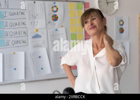 La femme mature masse son cou avec sa main, ressent une douleur intense et de la tension dans son bureau. Surmené et en bonne santé Banque D'Images