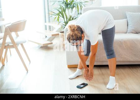 Femme de style de vie sain faisant l'entraînement de soins du corps à la maison dans un appartement confortable. Une femme faisant des exercices de fitness en intérieur regardant la classe d'entraîneur personnel sur le téléphone sur le sol. Cours de gym sur le web Banque D'Images