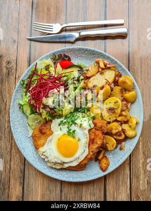 Pommes de terre frites avec oeuf frit sur schnitzel servi comme repas chaud avec une salade d'accompagnement sur une assiette avec des couverts à côté, Prerow, Mecklembourg-Poméranie occidentale, Allemagne Banque D'Images