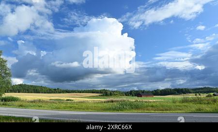 Un paysage rural pittoresque avec de vastes champs sous un ciel spectaculaire rempli de grands nuages moelleux. Une route traverse le premier plan, wi Banque D'Images