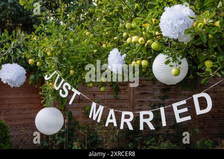 Une guirlande avec des lettres blanches et l'inscription Just Married pend à un pommier avec des pommes vertes et des lanternes blanches dans un jardin, préparations et décoration pour un mariage d'été dans le jardin Banque D'Images