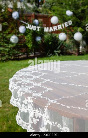 Nappe festive sur table au premier plan avec une bannière blanche et deux mots anglais en lettres majuscules JUSTE MARIÉES en arrière-plan, préparations pour un mariage de jardin, mariage en été Banque D'Images