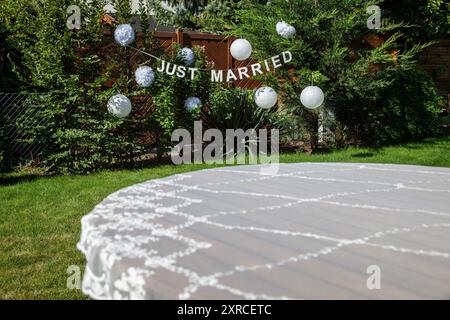 Nappe festive sur table au premier plan avec une bannière blanche et deux mots anglais en lettres majuscules JUSTE MARIÉES en arrière-plan, préparations pour un mariage de jardin, mariage en été Banque D'Images