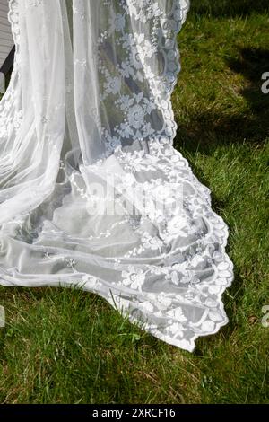 Une étole blanche transparente avec dentelle est étalée au soleil dans le jardin, préparation et sélection pour un mariage à la campagne Banque D'Images