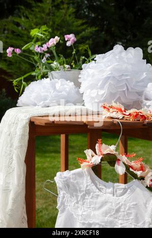 Gros plan d'une robe d'enfant blanche avec de la dentelle et une couronne de fleurs comme coiffe accrochée à un cintre à la table, préparations pour un mariage, préparation de mariage à l'extérieur Banque D'Images