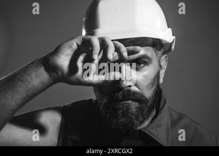 Constructeur fatigué dans le casque de sécurité. Travail acharné sur le chantier de construction. Un travailleur industriel fatigué essuie la sueur du front. Profession lourde. Architecte masculin Banque D'Images