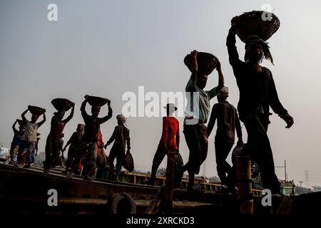 Une chaîne humaine de porteurs transporte du charbon, du sable et du gravier depuis les barges amarrées à la station d'atterrissage d'Aminbazar, sur le fleuve Buriganga, à l'extérieur de Dhaka. Le Bangladesh est diplômé de la catégorie des PMA (pays les moins avancés), grâce en grande partie au travail extrêmement difficile de la main-d'œuvre manuelle bon marché. Un porteur fait entre 80 et 140 USD par mois, selon les sites paylab.com et averagesalarysurvey.com Banque D'Images