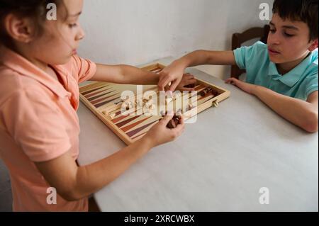 Deux enfants jouissant d'une partie de backgammon à la maison, se concentrant sur la stratégie et les compétences tout en s'amusant ensemble. Banque D'Images