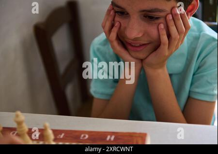 Un jeune garçon se concentre intensément sur un échiquier, contemplant son prochain mouvement. L'image capture un moment de concentration et de stratégie dans un set à la maison Banque D'Images