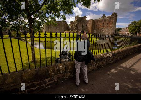 Rothesay, Bute, Écosse, Royaume-Uni. 6 juillet 2024. Un visiteur âgé prend une photo au-dessus de la clôture. Le château de Rothesay sur l'île de Bute est unique parmi les châteaux écossais à la fois pour sa date précoce et son plan circulaire inhabituel. Il est également célèbre pour ses liens étroits avec les Stewarts, à la fois alors qu'ils étaient hauts commissaires héréditaires et, à partir de 1371, une dynastie royale. À ce jour, l'héritier du trône a toujours le titre de duc de Rothesay. (Crédit image : © Ruaridh Stewart/ZUMA Press Press Press Wire) USAGE ÉDITORIAL SEULEMENT! Non destiné à UN USAGE commercial ! Banque D'Images