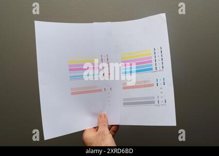 Une main masculine tient un papier test imprimé sur un fond gris, affichant plusieurs erreurs dans les barres colorées, indiquant des problèmes de performances de l'imprimante Banque D'Images
