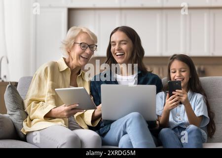 Joyeuse grand-mère, maman et fille d'enfant tenant des appareils numériques Banque D'Images