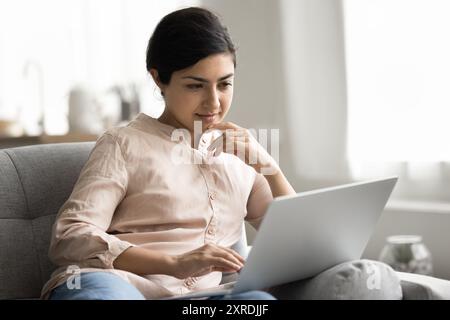 Femme indienne pensive apprendre le programme d'étude en ligne assis sur le canapé Banque D'Images