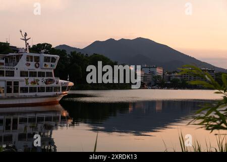 Lac Akan, Japon - 23 juillet 2024 : le soleil se couche sur un bateau de croisière sur le lac Akan et la station balnéaire onsen dans le parc national Akan-Mashu à Hokkaido in Banque D'Images