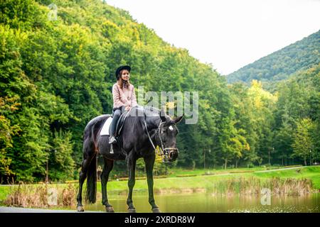 Petite fille à cheval en été. Enfant fille monte à cheval à l'extérieur au milieu de la forêt, parc, arbres, montagnes. Fille sur un cheval dedans Banque D'Images