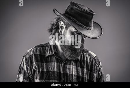 Chapeau de cow-boy en cuir. Beau jeune homme ajustant son chapeau de cow-boy. Homme non rasé cow-boys. Cow-boy américain. Style cow-boy dans une chemise à carreaux. Noir et blanc Banque D'Images