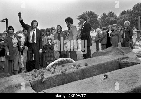 Les funérailles de Blair Peach, un enseignant de l'est de Londres, tué en avril 1979 lors d'une manifestation anti-Front national à Southall, dans l'ouest de Londres. Au cimetière, un deuil tient la main de ses filles, lève le poing en défiance et comme dernier geste de camaraderie. Des œillets rouges profonds à tige unique sont jetés sur la tombe, alors que les membres de la communauté asiatique attendent leur tour pour dire adieu. Blair Peach était un membre actif de la Ligue anti-nazie et de l'Inner London Teachers Association. Southall, Londres, Angleterre 13 juin 1979. HOMER SYKES des années 1970 Banque D'Images