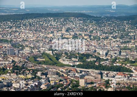 Weitläufiger Blick vom Uetliberg auf die Stadt Zürich Das Bild zeigt eine weitläufige Aussicht vom Uetliberg auf die Stadt Zürich. IM Vordergrund erstreckt sich die dichte Bebauung der Stadt mit einer Mischung aus Wohnhäusern, Bürogebäuden und Industriegebieten. Zahlreiche markante Gebäude und Straßenzüge sind deutlich erkennbar, darunter einige Grüne Oasen, die sich durch die urbanen Bereiche ziehen. Weiter im Hintergrund erstrecken sich die dicht besiedelten Wohnviertel Zürichs bis hin zu den bewaldeten Hügeln am Horizont, die die die Stadt umgeben. Diese Perspektive bietet einen umfassenden Übe Banque D'Images