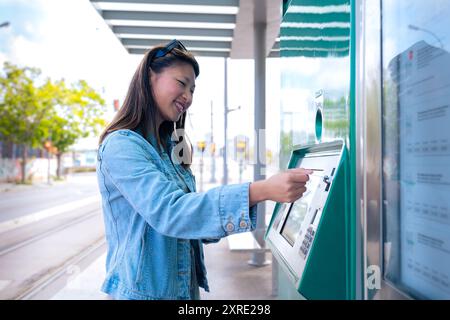 Jeune femme achetant un billet pour les transports publics à la machine automatique. Banque D'Images