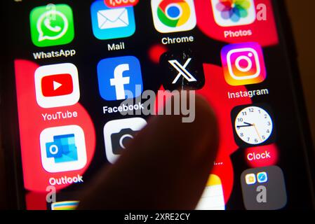 Gros plan de l'écran d'un smartphone affichant des applications de médias sociaux populaires, y compris Facebook, Instagram, WhatsApp et l'application X avec le doigt prêt à appuyer Banque D'Images