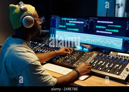 Ingénieur du son afro-américain utilisant une console de mixage et un ordinateur dans un studio d'enregistrement avec un équipement audio avancé et un logiciel d'édition Banque D'Images