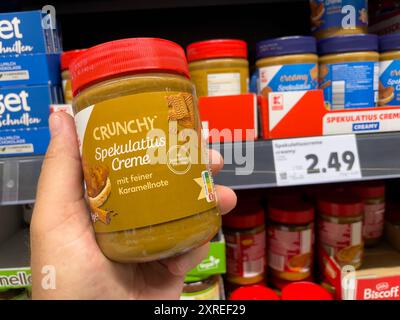 Un homme tient un pot de beurre d'arachide croquant dans un supermarché. Une variété de produits sont disponibles. Banque D'Images