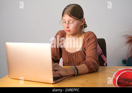 Retour à l'école. Devoirs. Adolescente avec des lunettes dans l'apprentissage à distance s'assoit Banque D'Images