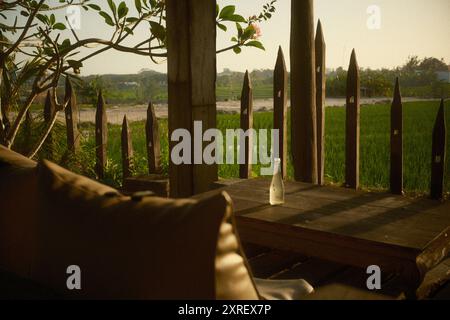 Une terrasse patio en bois équipée de meubles de jardin, y compris une chaise de sac de haricots et une table rustique en bois, avec une vue sur les rizières, frangip Banque D'Images