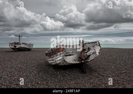 Image partiellement désaturée de deux vieux bateaux de pêche côtiers à coque en bois terminent leurs journées sur la plage de galets d'Aldeburgh, dans le Suffolk. Vue sur la côte. Banque D'Images