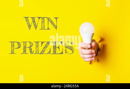 Une personne tenant une ampoule avec les mots « gagner des prix » écrits en arrière-plan. Concept d'excitation et de réalisation, comme si la personne tenant t Banque D'Images