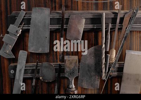 Divers outils de travail du bois accrochés soigneusement sur un mur en bois, présentant des outils traditionnels et modernes. Les outils comprennent des ciseaux, des rabots et des couteaux à découper Banque D'Images